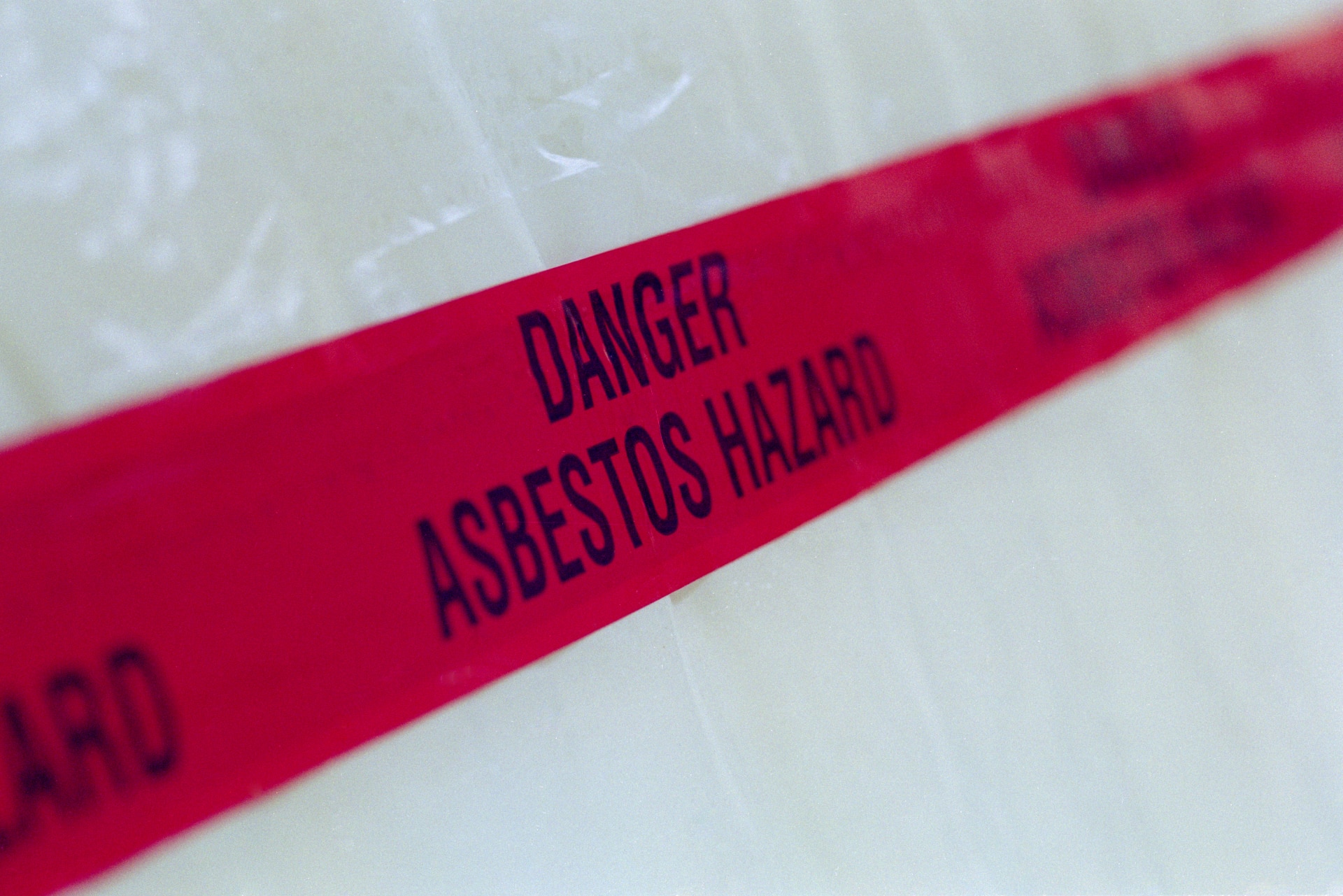 Caution tape reading “Danger Asbestos Hazard” blocking off work around a restoration site.